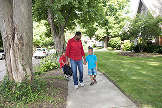 A man walks to children to school on a sidewalk.